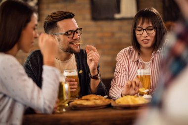 Happy couple drinking beer and eating tortilla chips with friends in a pub. 