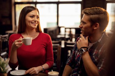 Young happy couple talking to each other while drinking coffee in a cafe. Focus is on woman. 
