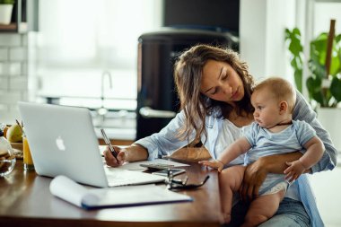 Young working mother planning home budget while being with her baby at home. 