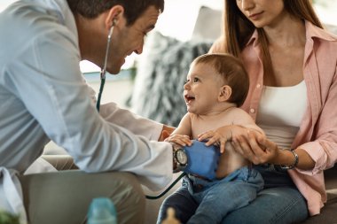 Happy baby boy having fun while doctor is listening his heartbeat with a stethoscope.