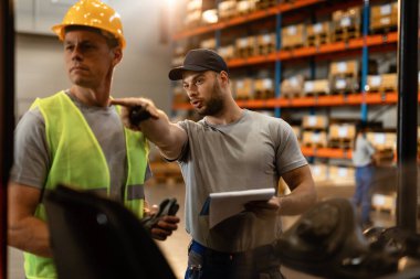 Warehouse dispatcher talking with a worker in industrial storage compartment. 