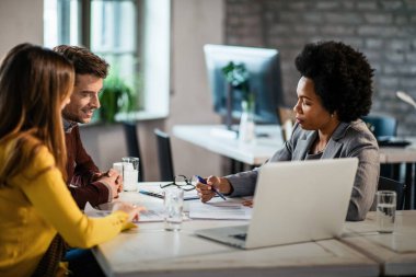 African American real estate agent and couple going through terms of a contract while having a meeting in the office. 