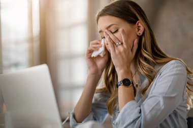 Young businesswoman with cold and flu virus having a headache while working in the office. 
