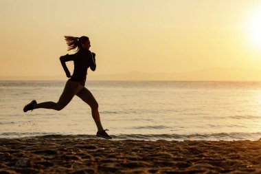 Full length of motivated athletic woman running at the beach at sunset. Copy space. 