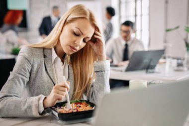 Pensive businesswoman eating vegetable salad during her lunch break in the office. 