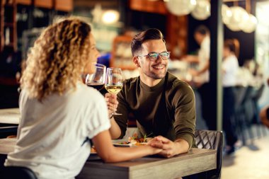 Young loving couple holding hands and drinking wine while eating in a restaurant. 