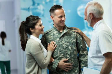Happy senior doctor communicating with military man and his wife after the appointment in the hospital. 