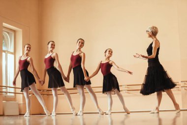 Group of happy ballerinas holding hands while having ballet class with their teacher.at dance studio. 