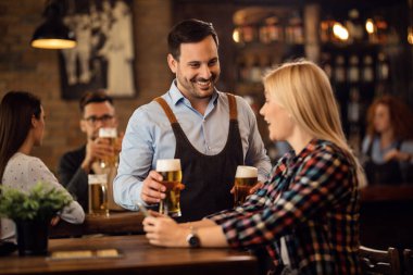 Happy waiter is serving a woman with glass of beer in a pub. 