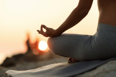 Close-up of woman in lotus position meditating at sunset. 