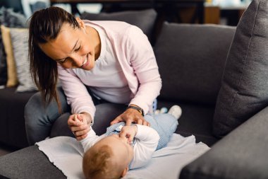 Happy mother playing with her baby boy who is lying on the sofa. 