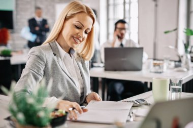 Happy businesswoman reading notes from her weekly planner while working in the office.