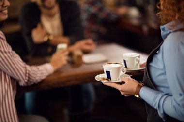 Unrecognizable waitress working in a cafe ad serving her customer with a coffee. 