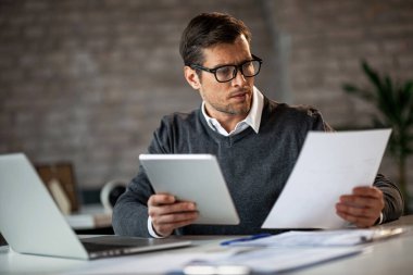 Businessman reading reports and using touchpad while working in the office. 