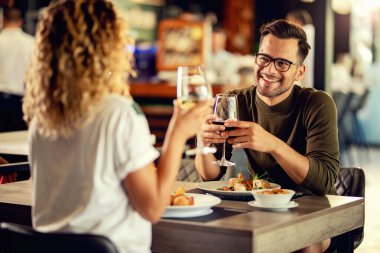 Young happy man communicating with his girlfriend while having a lunch and drinking wine in a restaurant. 