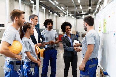 African American company leader visiting employees in a factory and shaking hands with one of the workers. 