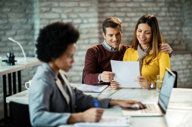 Happy couple having a meeting with insurance agent and reading financial plans together. 