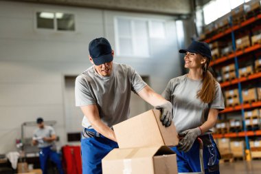Warehouse workers cooperating while preparing cardboard boxes for distribution in industrial building. 