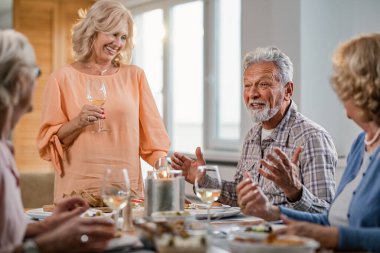 Group of mature friends having fun while communicating during lunch at home. Focus is on a man. 