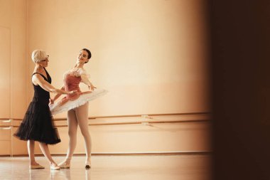 Mature ballet teacher teaching young ballerina during rehearsal at dance studio. Copy space.