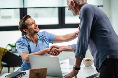Smiling doctor greeting a mature patient and shaking hands with him at medical clinic. 