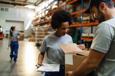 Two workers examining cardboard box before the shipment while working in a warehouse. Focus is on African American woman. 