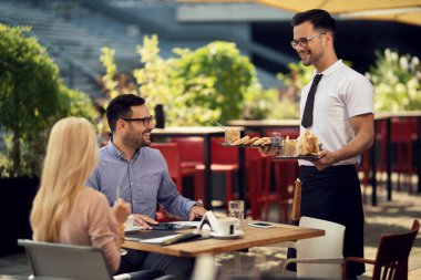 Happy waiter serving a meal to a couple during lunch time in a restaurant. 