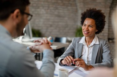 Happy black insurance agent communicating with her clients while having a meeting in the office. 