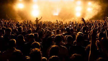 Rear view of large group of people having fun at music concert while watching live performance on the stage. 