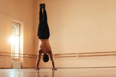 Back view of male ballet dancer doing handstand while exercising in ballet studio. Copy space. 