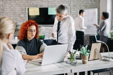 Annoyed businesswoman working on the computer while her executive manager in looking at her in the office. 