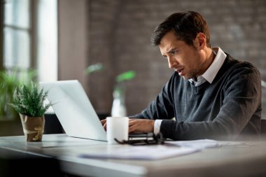 Serious businessman using computer and typing something while working in the office. 