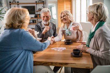 Happy senior women handshaking after playing cards with their friends at home. 