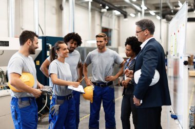 Happy factory worker and her colleagues showing business reports to company leaders while having a meeting in industrial plant.