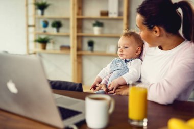 Mother and her baby boy using laptop while relaxing at home. 