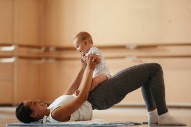 Happy athletic mother having fun with her baby while doing post-pregnancy exercises on the floor. 