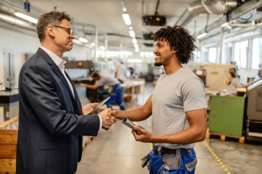 Happy African American metal worker shaking hands with a manager in industrial building. 