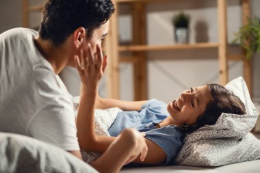Young couple having fun and laughing while relaxing on the bed. Focus is on woman. 