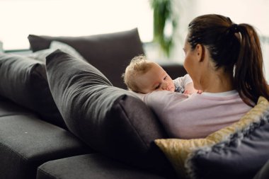 Cute baby and mother relaxing on the sofa at home. 