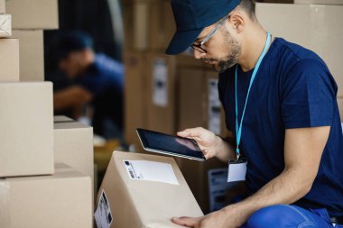 Young delivery man using touchpad and scanning bar code on a label of cardboard box in a van. 