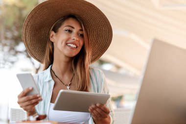 Young multi-tasking woman reading an e-mail on laptop while using touchpad and cell phone in a cafe.  
