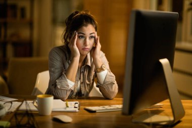 Young woman feeling confused while working late and reading something on a computer at home. 