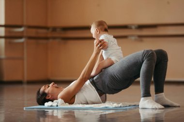 Cheerful mother working out and having fun with her baby in health club. 