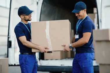 Two delivery men loading cardboard boxes in a mini van. 