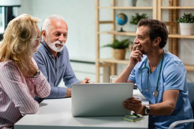 Happy mature couple communicating with their doctor while using laptop together. Focus is on doctor. 