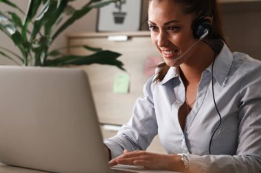 Happy female customer support representative talking to a customer and working on a computer in the office. 