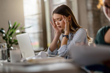 Young businesswoman feeling exhausted from work and holding her head in pain in the office. 