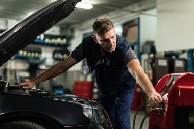 Mid adult mechanic doing service of car's air conditioner unit in auto repair shop. 