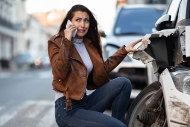 Young woman feeling desperate after a car accident and calling for road assistance over cell phone. 