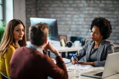 Black female insurance agent communicating with a couple and going through paperwork during the meeting. 